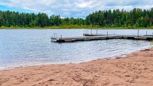 A sandy beach with a wooden dock extending into a calm lake, surrounded by dense green forest. - 5 Person Holiday Home in Bockara (Bockara)