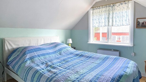 Een enkel bed met een gestreept dekbedovertrek in een kamer met een schuine plafond en een raam met gordijn.