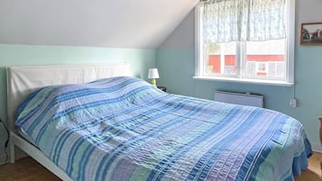 Una cama individual con una colcha a rayas en una habitación con techo inclinado y ventana con cortina.