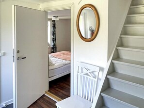 A bedroom with a bed, a white chair, a wooden-framed mirror, and a staircase. - 5 Person Holiday Home in Bockara (Bockara)