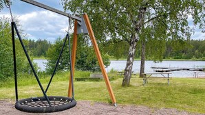 Een schommel met een autobandschommel, picknicktafels en een meer op de achtergrond.
