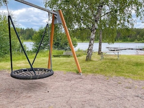 A swing set with a tire swing, picnic tables, and a lake in the background. - 5 Person Holiday Home in Bockara (Bockara)