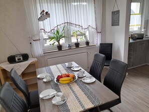 Een eetgedeelte met een tafel voor vier personen, stoelen, een potplant en een radiator.