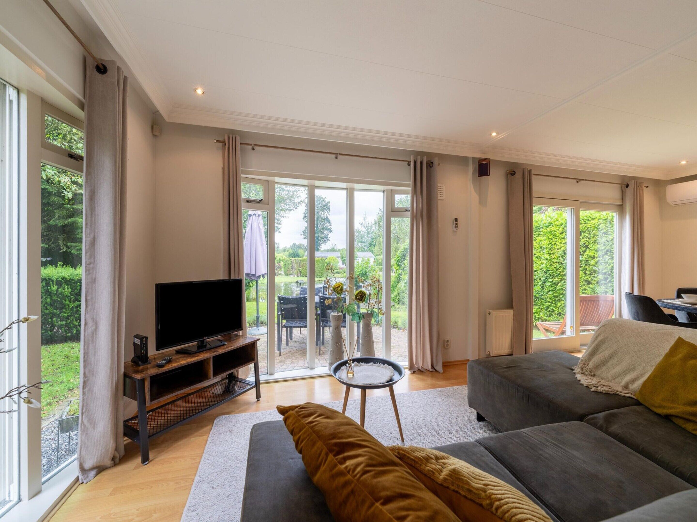 Een ruime woonkamer met een grote televisie, comfortabele zitplaatsen en uitzicht op de tuin via glazen deuren.