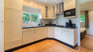 A modern kitchen with white cabinets, a black microwave, and a window with greenery outside. - Holiday Home in Overijssel Near Cap Fun Park (Rheezerveen)