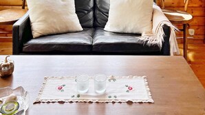 A cozy room with a black leather sofa, two white pillows, a wooden table with a lace tablecloth, two glasses, and a small bowl. - 5 Person Holiday Home in Sodertalje (Sodertalje)