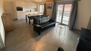 A spacious living area with a black leather sofa, a dining table, and a kitchen in the background. - Cozy Fisherman's House With Garden (Koksijde)