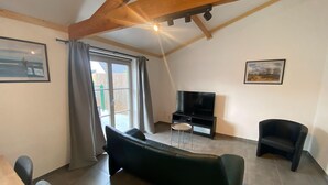 A living room with a sofa, a TV, and a chair. There is a window with curtains and a door. - Cozy Fisherman's House With Garden (Koksijde)