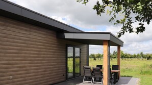 Ein modernes Gebäude mit überdachter Außenbestuhlung, großen Fenstern und Blick auf eine Wiese.