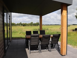 An outdoor patio with a table and chairs, a covered area, and a view of a grassy field. - Spacious Chalet in a Rural Location Near Giethoorn (Blesdijke)