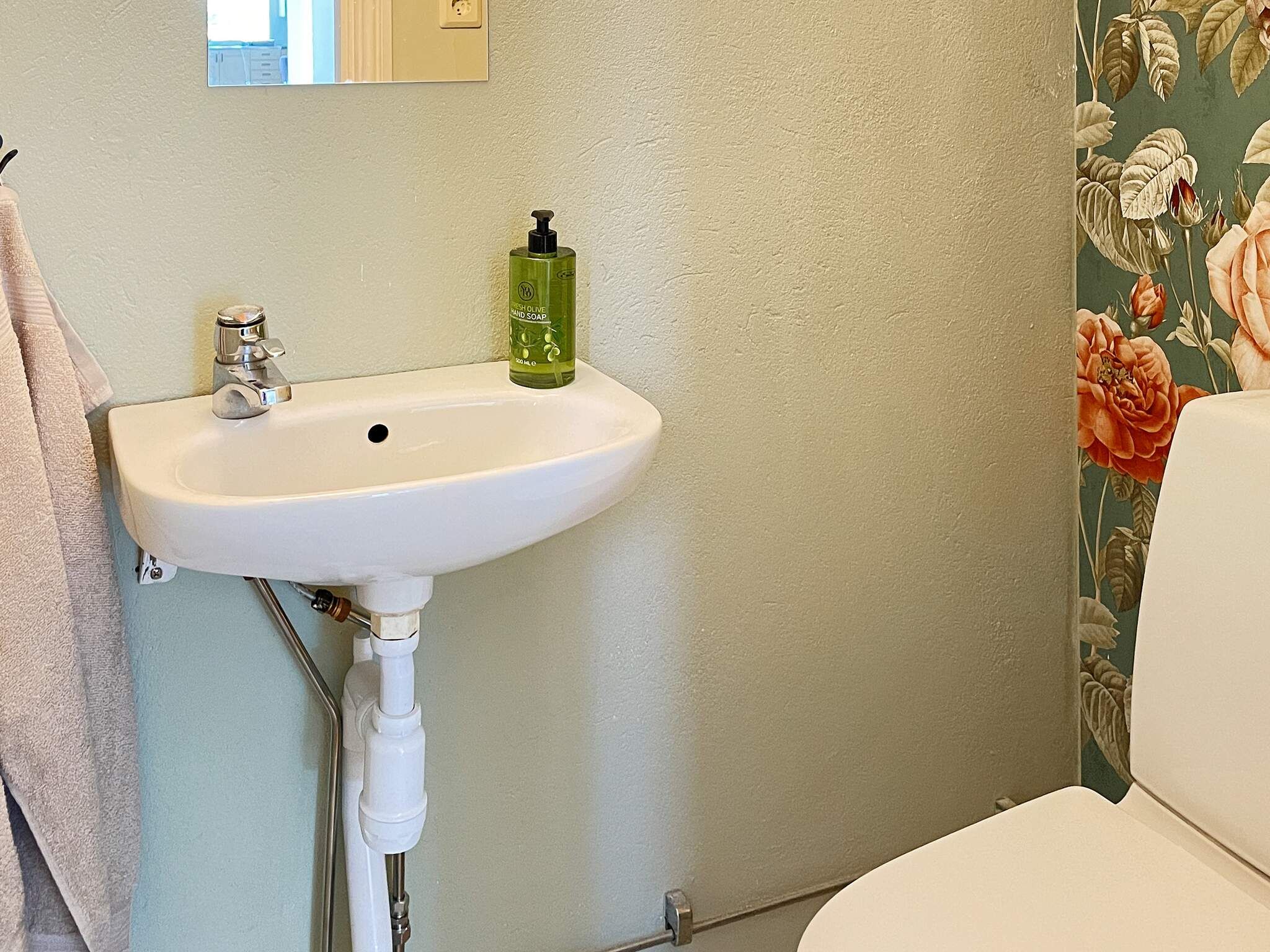 A bathroom with a white sink, a green soap dispenser, and a toilet.