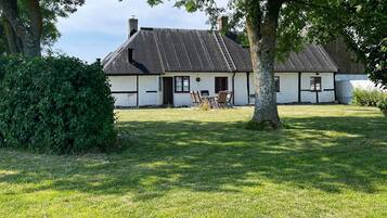 A traditional house with a sloped roof, a front porch with chairs, and a well-maintained lawn.