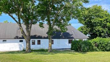 A white building with a grey roof, surrounded by green grass and trees.