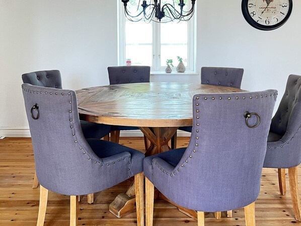 A round wooden dining table with six upholstered chairs, each with a metal ring on the backrest. - 8 Person Holiday Home in Skivarp (Skivarp)
