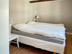 A single bed with a white mattress and gray bedding, a white bedside table, and a white lamp. - 8 Person Holiday Home in Skivarp (Skivarp)