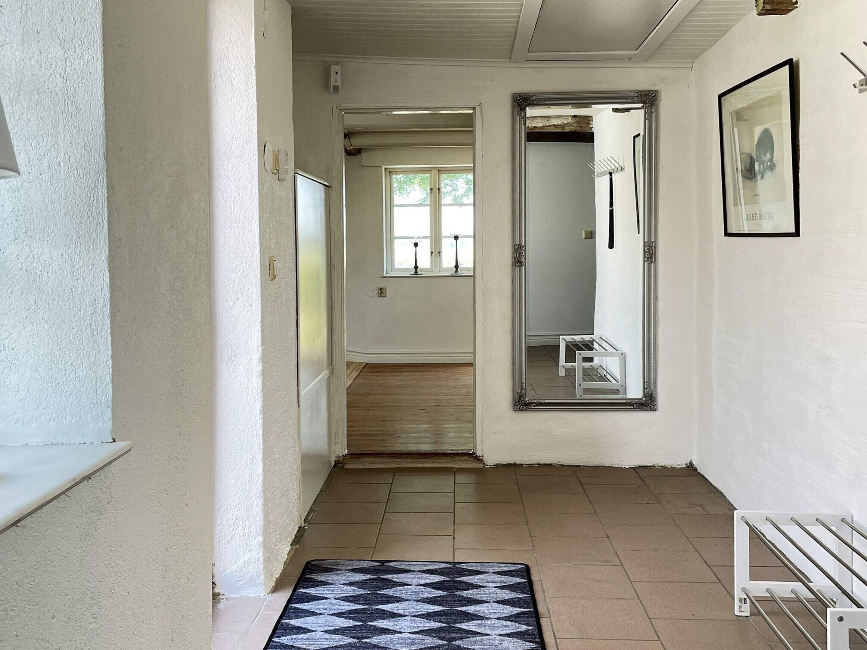 A hallway with a door leading to a bathroom, a mirror, and a framed picture on the wall.