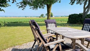 An outdoor wooden table and chairs set on a gravel surface with a view of a green field and a tree. - 8 Person Holiday Home in Skivarp (Skivarp)