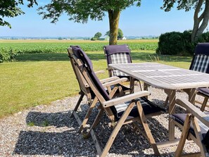 An outdoor wooden table and chairs set on a gravel surface with a view of a green field and a tree. - 8 Person Holiday Home in Skivarp (Skivarp)