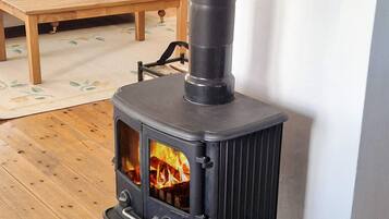 A wood-burning stove with a glass door, a wooden table with candles, and a chair in a living room.