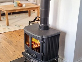 En vedeldad kamin med en glaslucka, ett träbord med ljus och en stol i ett vardagsrum.