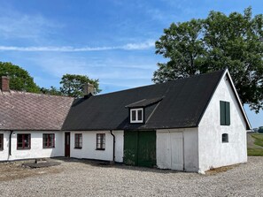 Un edificio blanco con techo negro, una puerta verde y una ventana pequeña.