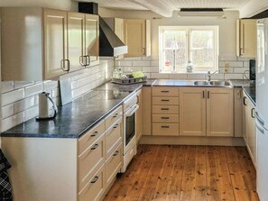 A kitchen with wooden flooring, white cabinetry, a stainless steel range hood, and a window providing natural light.