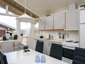 A modern kitchen with white cabinets, a stove, and a dining area with a table and chairs. - 5 Person Holiday Home in Aabenraa (Aabenraa)