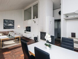 A modern living room with a fireplace, a sofa, a dining table with chairs, and a large window.