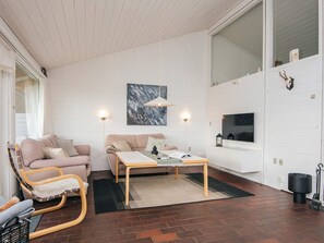 A modern living room with a sofa, a rocking chair, a coffee table, and a TV mounted on the wall. - 5 Person Holiday Home in Aabenraa (Aabenraa)