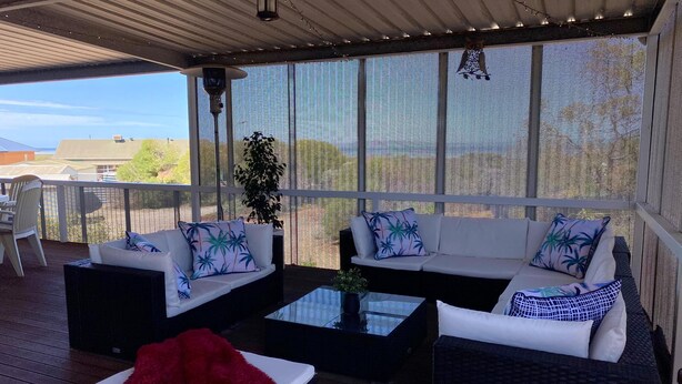 A covered outdoor seating area with a sofa set, a coffee table, and a red chair.