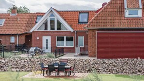 A residential building with a red brick facade, a red garage door, and a patio area with outdoor furniture. - Torbogenhuus No. 5 Comfortable Holiday Residence (Norderney)