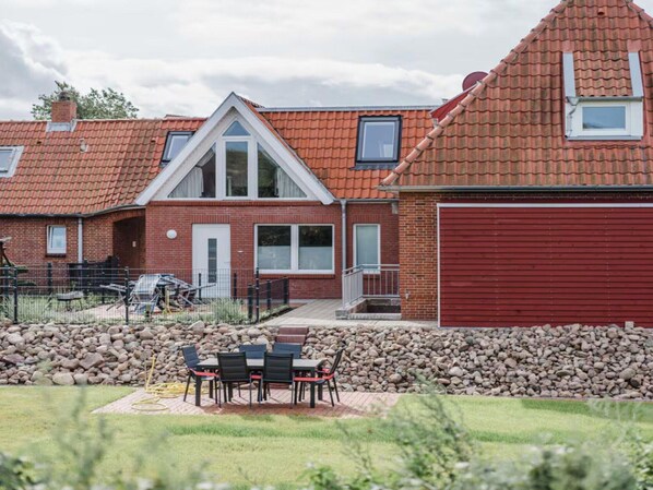 Een woongebouw met een rode bakstenen gevel, een rode garageklep en een terras met tuinmeubilair.