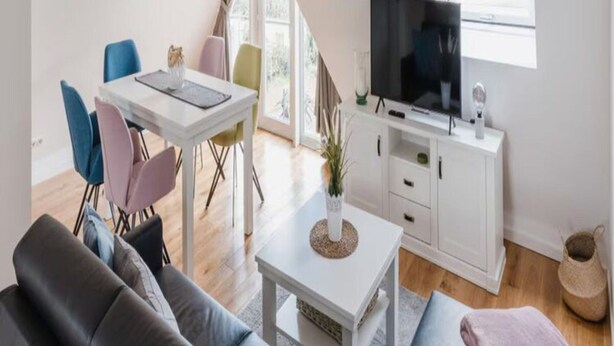 A modern living room with a white TV stand, a dining table with colorful chairs, and a sofa. - Torbogenhuus No. 5 Comfortable Holiday Residence (Norderney)