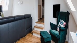 A modern living room with a dark sofa, a green armchair, and a wooden staircase leading to an upper level. - Torbogenhuus No. 5 Comfortable Holiday Residence (Norderney)