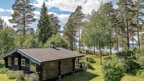 A rustic cabin with a tiled roof, surrounded by dense forest and a lake. - 4 Star Holiday Home in Yxlan (Yxlan)