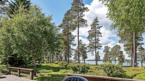 A deck with a chair and a table, overlooking a lake with tall trees and a clear sky. - 4 Star Holiday Home in Yxlan (Yxlan)