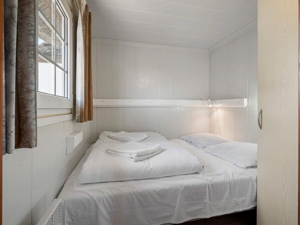 Une petite chambre avec un lit simple, des murs blancs et une fenêtre avec des rideaux.