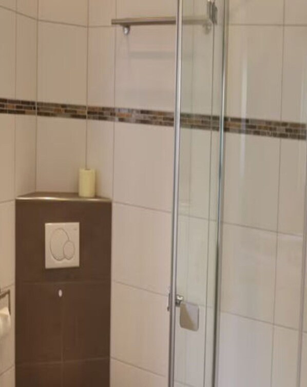 Une salle de bain dotée d’une douche à parois de verre, d’un distributeur de serviettes et d’un thermostat fixé au mur.
