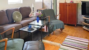 A living room with a brown sofa, a green armchair, a glass coffee table, and a television on a wooden stand. - 6 Person Holiday Home in Kattarp (Kattarp)