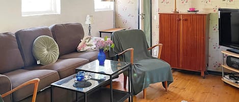 A living room with a brown sofa, a green armchair, a glass coffee table, and a television on a wooden stand.