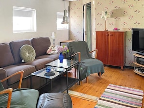 A living room with a brown sofa, a green armchair, a glass coffee table, and a television on a wooden stand. - 6 Person Holiday Home in Kattarp (Kattarp)