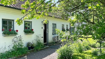 A white building with a gravel path leading to a door, surrounded by greenery and potted plants.