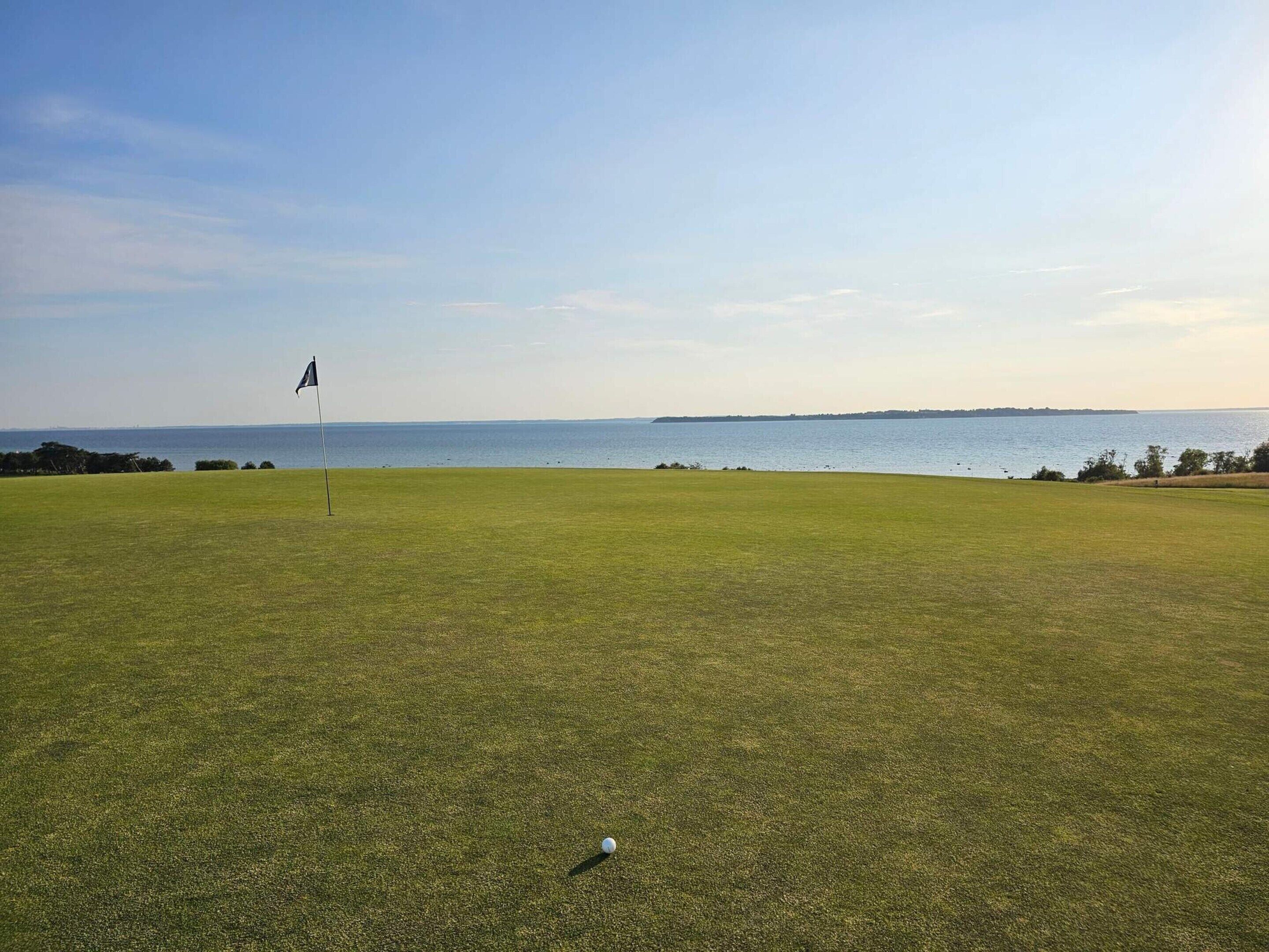 A golf course with a flagstick and a golf ball on the green, overlooking a body of water.