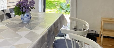 A dining area with a table covered by a patterned tablecloth, two chairs, and a vase with flowers.