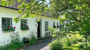 A white house with a gravel path leading to the entrance, surrounded by greenery and potted plants. - 6 Person Holiday Home in Kattarp (Kattarp)