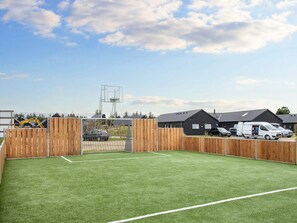 En inhägnad sportplan med ett mål, omgiven av byggnader och parkerade fordon.