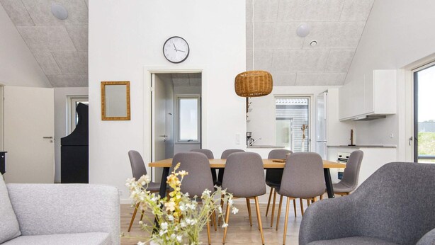 Una sala moderna con un sofá, una silla, una mesa de comedor con sillas, un jarrón con flores y un reloj en la pared.