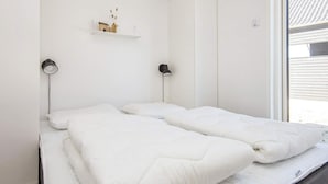 Una habitación con una cama, dos lámparas de pared, una estantería con objetos decorativos y una ventana.