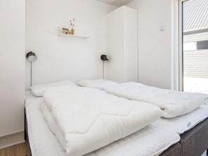 Een kamer met een bed, twee bedlampen, een plank met decoratieve objecten en een raam.