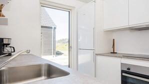Una cocina moderna con armarios blancos, un lavamanos de acero inoxidable, una cafetera y un horno empotrado.